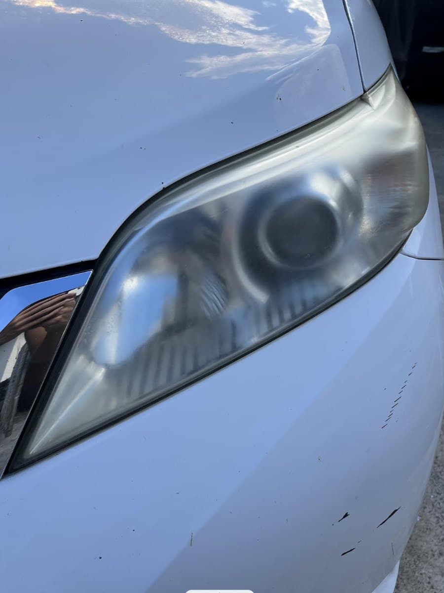 Hazy, yellowed headlight lens on a white car before restoration