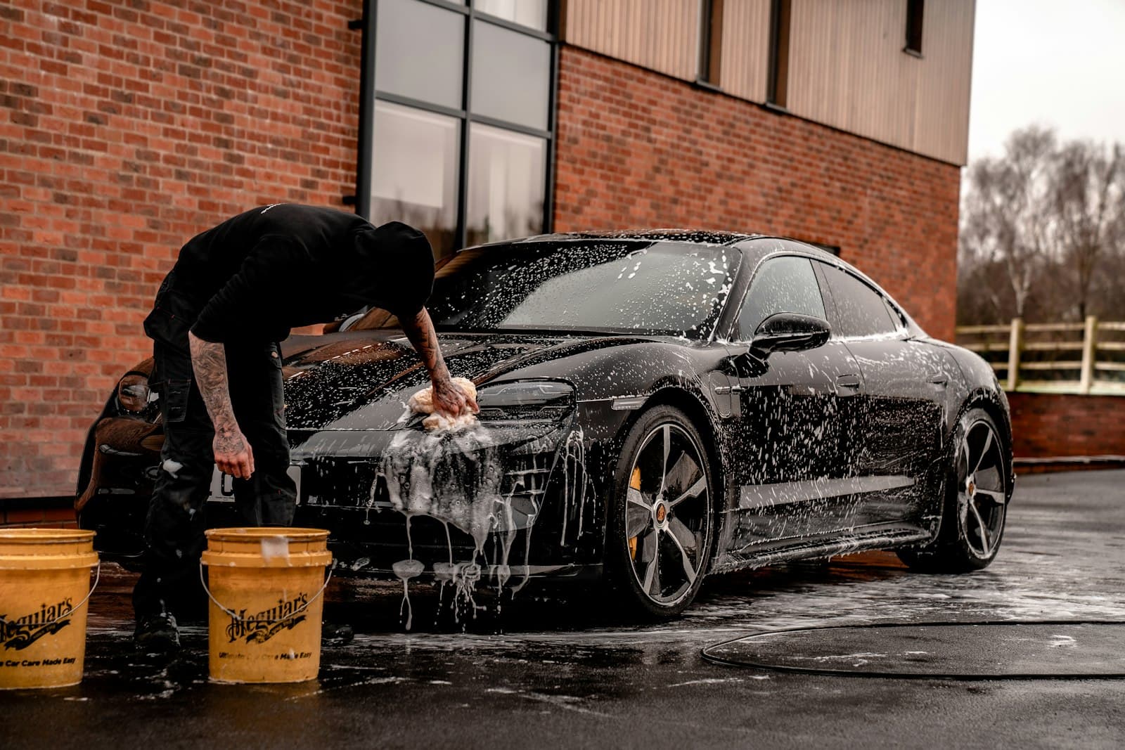 Detailer hand-washing a black car covered in thick foam